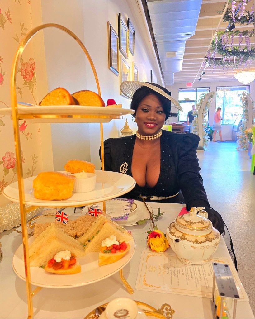Woman dressed in black enjoying a traditional high tea setup with finger sandwiches, scones, and a teapot at High Tea Grand Rapids