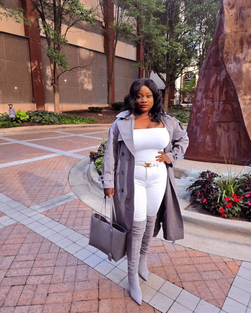 Chic fall outfit with grey trench coat, white fitted top, white jeans, grey suede thigh-high boots, and matching grey tote bag in a city setting.