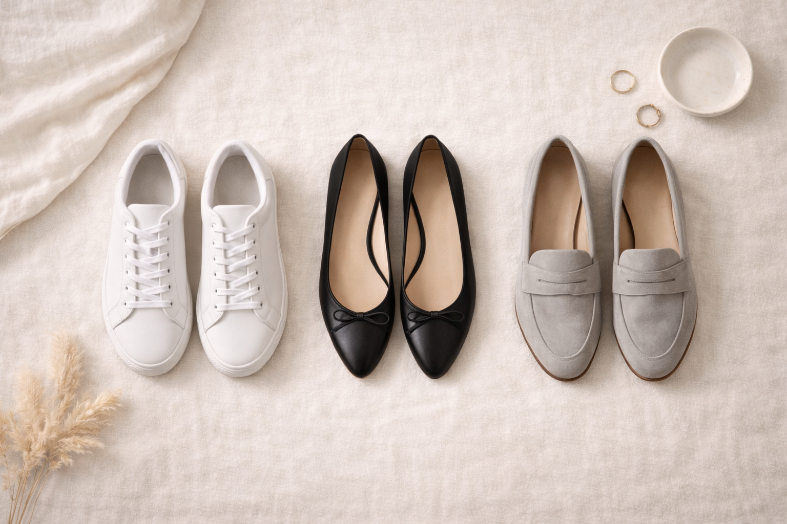 Capsule wardrobe shoes including white sneakers, black ballet flats, and grey loafers arranged neatly on a light background.